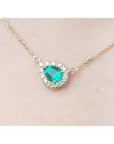Vibrant pear-shaped emerald necklace with diamond halo on a 14K yellow gold chain.