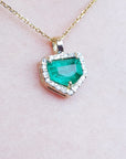 Gold necklace with a heart-shaped emerald pendant on a light pink background