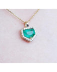 Gold necklace with a heart-shaped emerald pendant on a light pink background