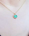 Necklace with a heart-shaped natural emerald pendant on a person wearing a dark blue top.