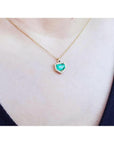Colombian emerald pendant with diamond halo on a thin 14K gold chain, worn on a person.