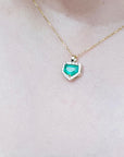 Gold necklace with a heart-shaped emerald pendant on a blurred background.