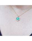 Gold necklace with a heart-shaped emerald pendant on a blurred background.