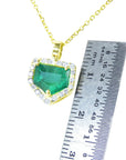 Gold necklace with a Muzo mine emerald pendant next to a ruler for size reference on a white background
