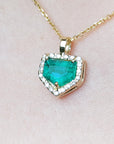 Gold necklace with a heart-shaped emerald pendant on a light pink background.