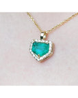 Gold necklace with a heart-shaped emerald pendant on a light pink background.
