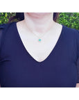14K gold pendant with a vibrant Colombian emerald and diamond halo, worn on a woman's neck.