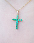 Gold cross necklace with genuine emeralds on a person's neck.