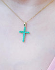 Gold necklace with a natural emerald cross pendant on a person wearing a pink top.
