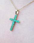 Yellow gold emerald cross pendant on a light pink skin background.