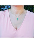 18K yellow gold necklace with a vibrant green emerald cross pendant on a woman's chest.