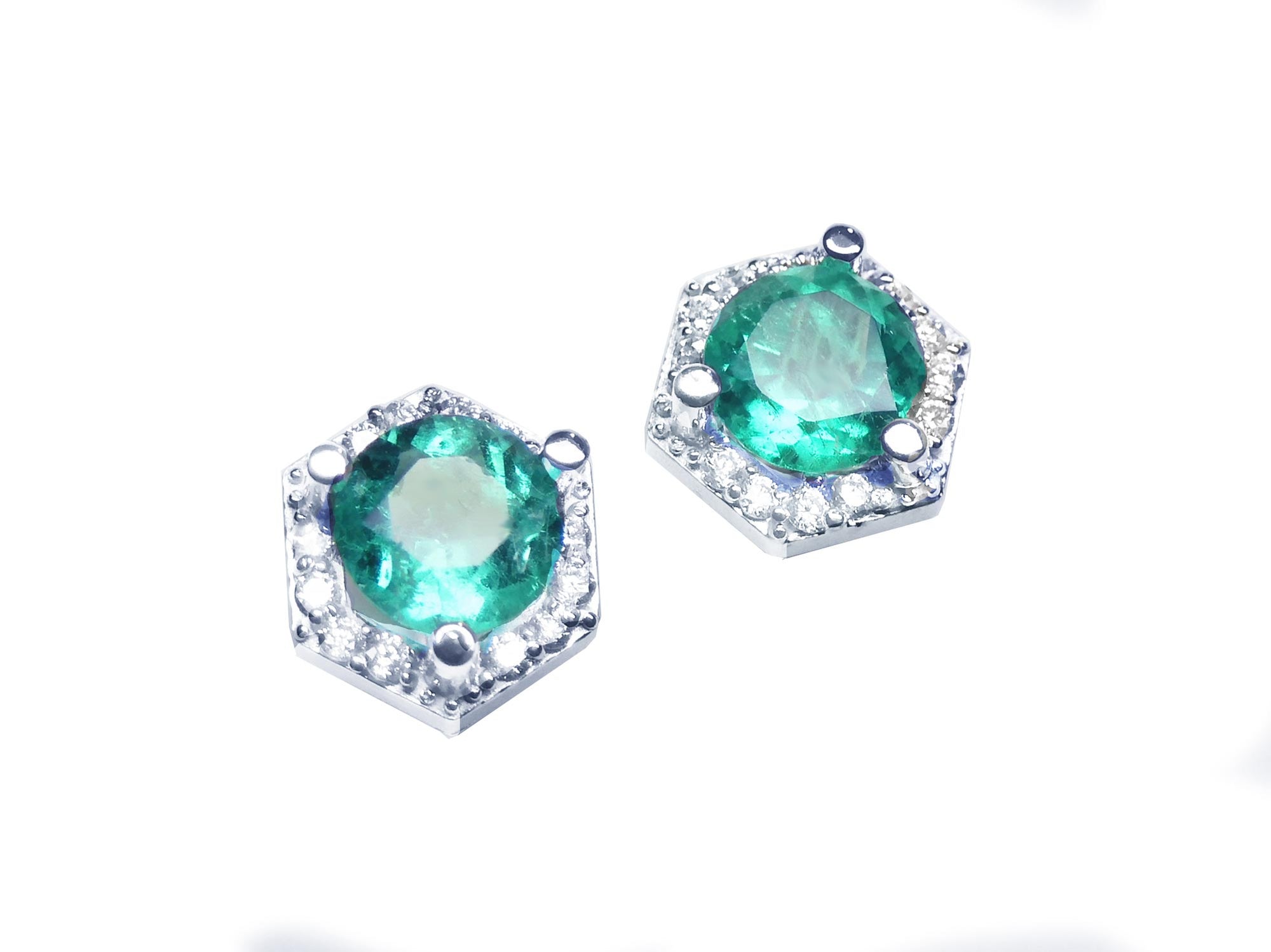Diagonal top view position of pair of hexagonal halo diamond emerald stud earrings white gold.