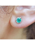 Close-up of an earlobe wearing an hexagonal halo diamond emerald stud earring.