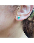 Emerald stud earring with hexagonal diamond halo in 14K white gold on an ear.