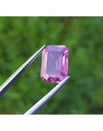 4.05 ct natural loose pink sapphire, emerald cut, held by tweezers against a green background.