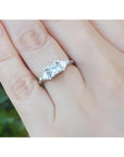 14K white gold ring with a princess cut center diamond and two trillion side diamonds on a hand.