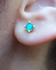 Close-up of an ear wearing a emerald stud earring with a blurred natural background.