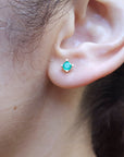 Close-up of an ear wearing a emerald stud earring with a blurred natural background.