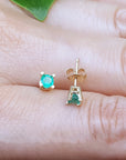 Gold earrings with round cut emeralds gemstones on a person's finger