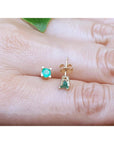 Gold earrings with round cut emeralds gemstones on a person's finger