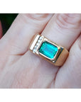 Men's 14K yellow gold ring with an east-west emerald-cut Colombian emerald and channel-set diamonds.