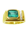 A yellow gold ring with a natural emerald bezel set and small diamonds on a topside view.