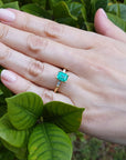 Hand wearing a natural emerald ring with leaves in the background.