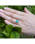 Hand wearing a natural emerald ring with leaves in the background.