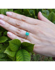 14K gold ring with a rectangular emerald-cut emerald and tapered baguette side diamonds on a hand.