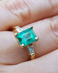 Gold ring with a natural Colombian emerald and side diamonds on a hand.