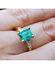 Gold ring with a natural Colombian emerald and side diamonds on a hand.