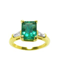A front top view of an emerald gold ring with tapered baguettes side diamonds on a white background.