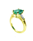 The half side of a gold emerald ring with a side diamond and band profile on a white background