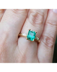 14K gold ring with a rectangular emerald-cut emerald and tapered baguette side diamonds on a hand.