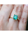 14K gold ring with a rectangular emerald-cut emerald and tapered baguette side diamonds on a hand.
