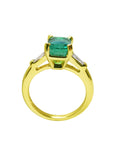 The lateral profile view of a gold emerald ring on a white background