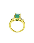 The lateral profile view of a gold emerald ring on a white background