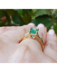 14K gold ring with a rectangular emerald-cut emerald and tapered baguette side diamonds on a hand.