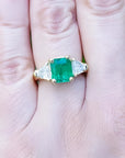 18K yellow gold ring with a GIA certified emerald and side trillion diamonds on a hand.