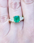 18K yellow gold ring with a GIA certified emerald and side trillion diamonds on a hand.