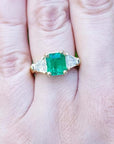 18K yellow gold ring with a GIA certified emerald and side trillion diamonds on a hand.