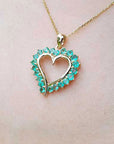 Heart-shaped pendant with emeralds gemstones on a gold chain against a light skin background.
