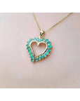 14K gold heart pendant necklace with vibrant green Colombian emeralds, worn on a person.