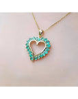14K gold heart pendant necklace with vibrant green Colombian emeralds, worn on a person.