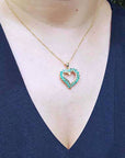 Heart-shaped pendant necklace with round cut emeralds on a person wearing a blue top.
