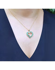 14K gold heart-shaped pendant necklace with vibrant green Colombian emeralds on a woman's chest.