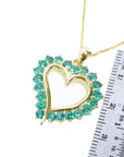 Gold heart-shaped pendant with round emerald stones next to a ruler for scale on a white background.