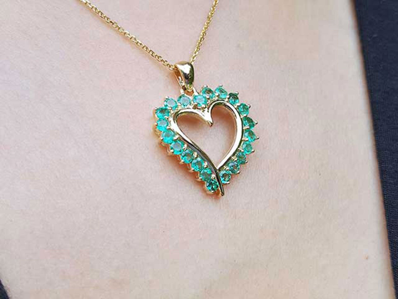 Heart-shaped emerald pendant on a gold chain against a neutral skin background.