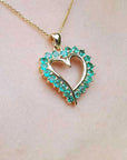 Heart-shaped emerald pendant on a gold chain against a neutral skin background.