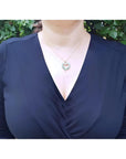 Woman wearing a 14K gold necklace with a heart-shaped emerald pendant.